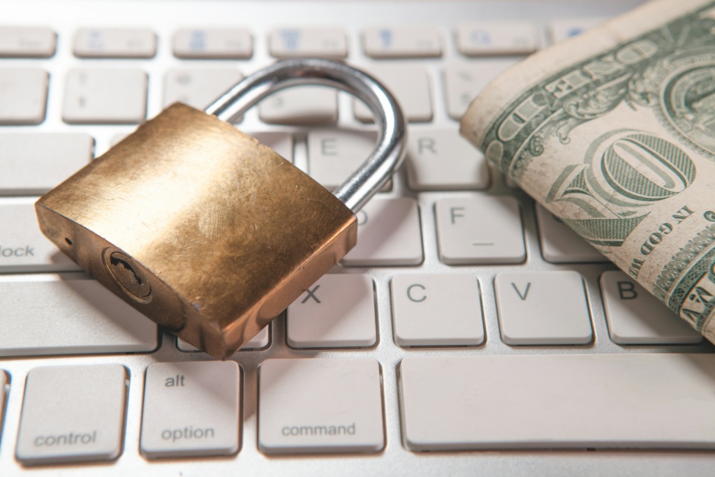 A padlock and dollar bills rest on a computer keyboard.